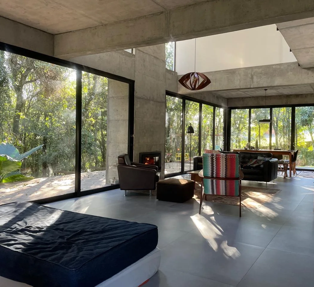 Sala da Casa 235 com concreto aparente, grandes planos de vidro e vista para a mata
