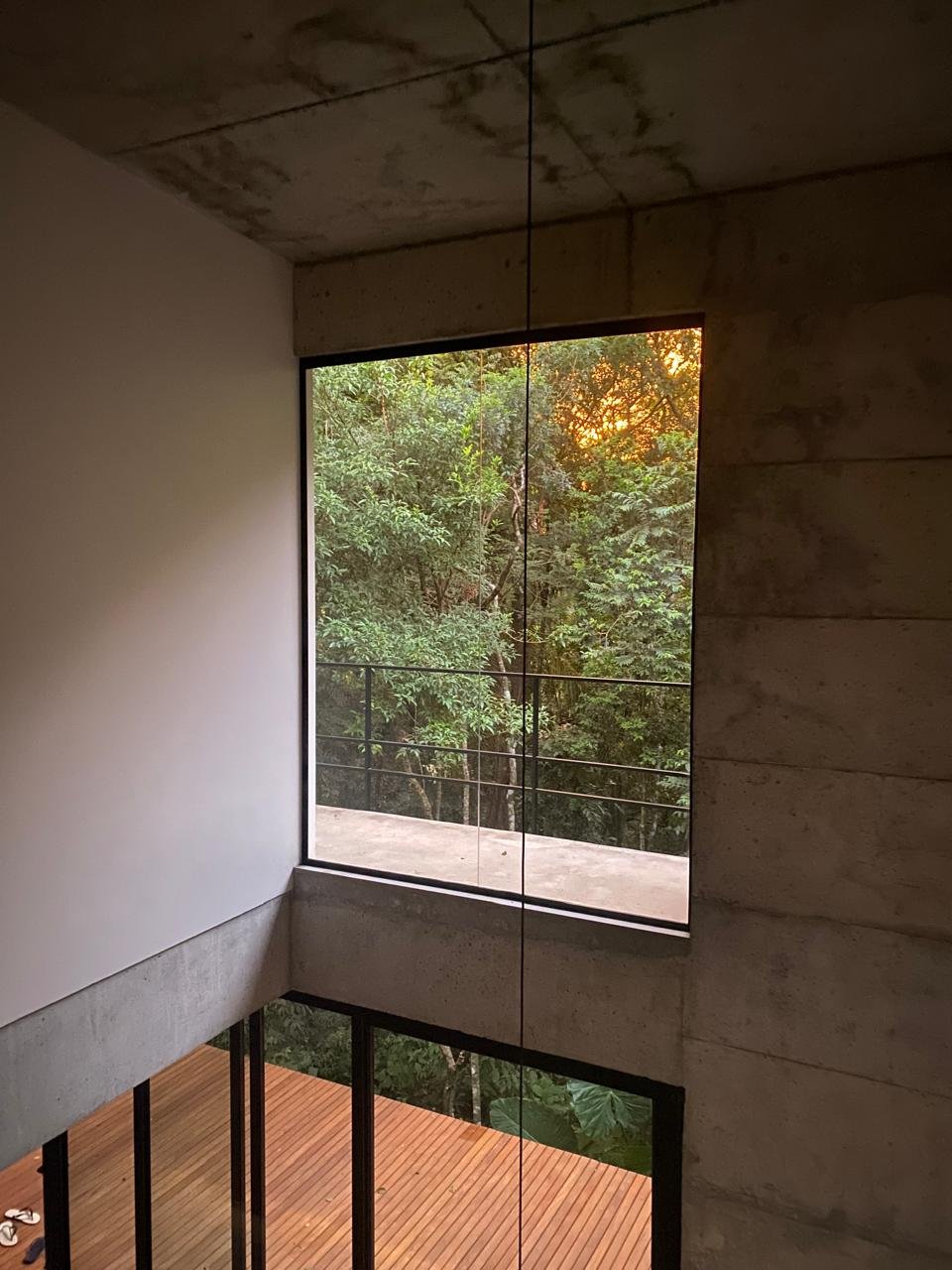 Interior da Casa 235 aberto para a mata, com concreto aparente e ampla esquadria